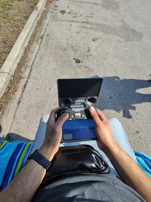 Hands working the drone controls beside a park.