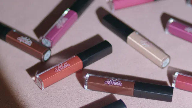 Lip gloss tubes scattered across pink paper in hard afternoon light.