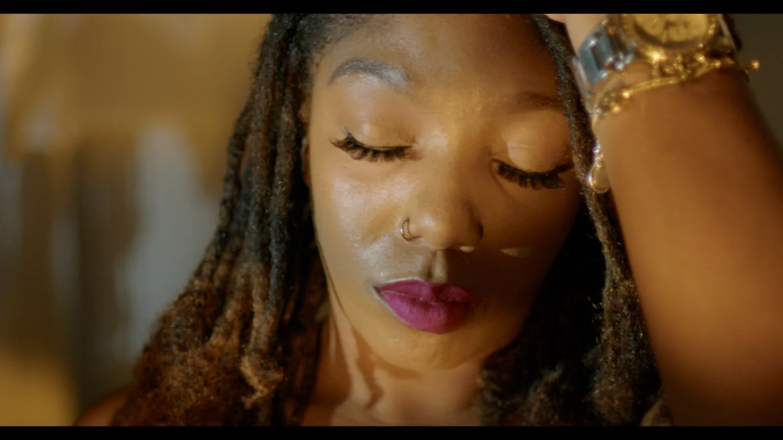 A woman with her hand in her hair and pink lipstick in warm light.
