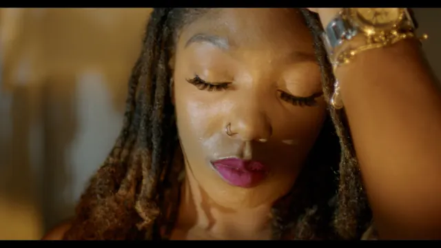 A woman with her hand in her hair and pink lipstick in warm light.
