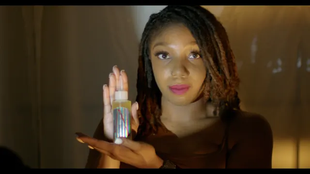 A woman holding lip gloss beside her face in golden light.