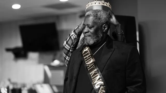 Black-and-white birthday portrait of a man wearing a crown and sash.