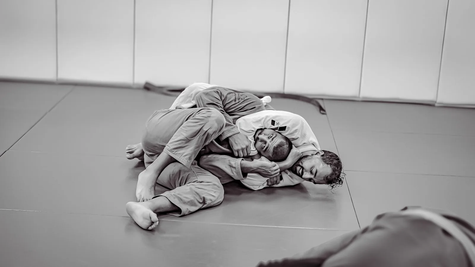 Two jiu-jitsu practitioners grappling on a mat in black and white.