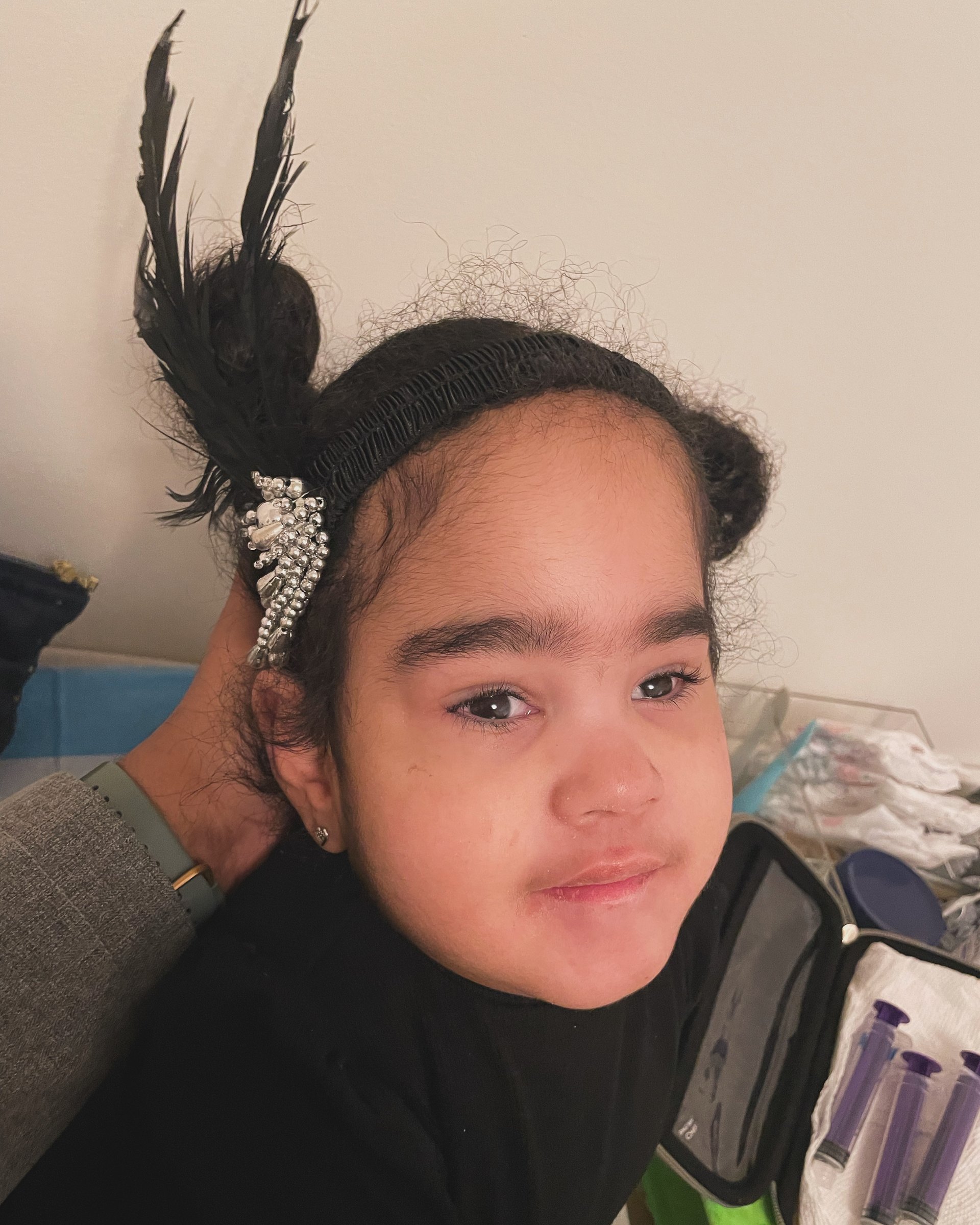 Havana at three, hair up with a feathered clip, looking straight at the camera.
