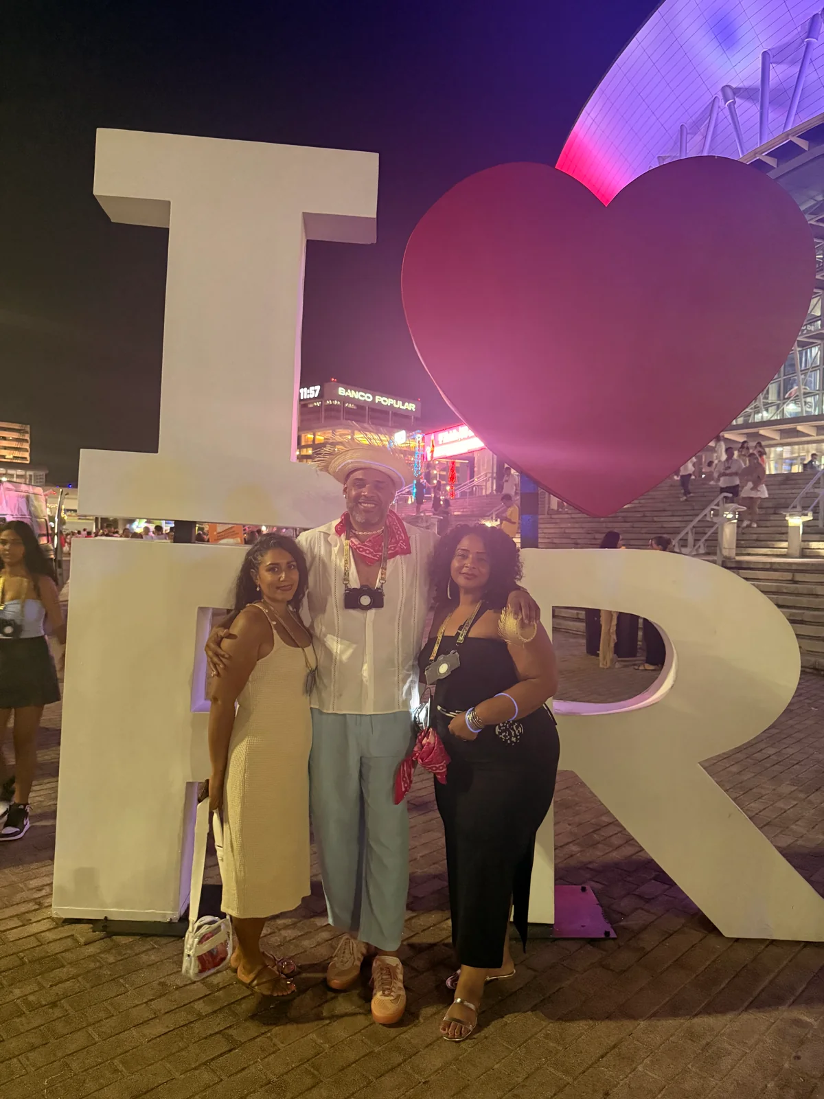 Falú with two companions beneath the illuminated I love PR sign.